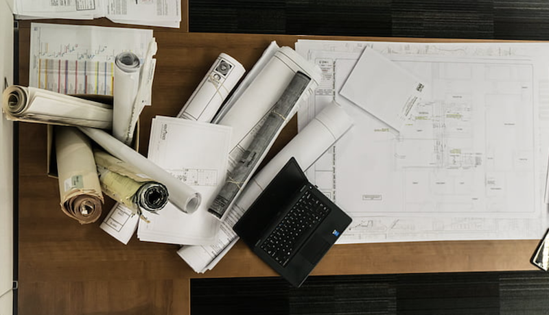 rolls of floor plans on wood desk with laptop