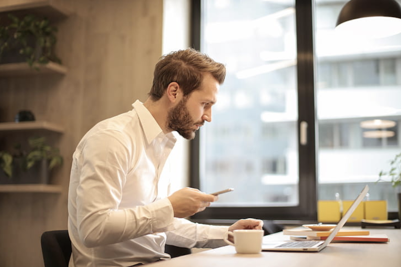 young man in office at his desk with laptop and cellphone