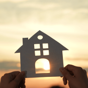 Hands holding up paper house cutout with sun shining through