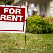 A "For Rent" sign sits in front of a single-family home. 