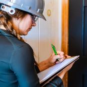 A woman in a gray hard hat takes notes at a jobsite