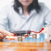 Coins are placed in ascending order from left to right. At the end of the row is a wooden model home, showing price changes in the housing market.