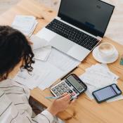 A renter looks over budget with laptop, bills, and calculator at a table