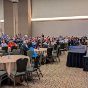 Professional builders in large room listening to speaker on stage