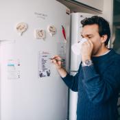 Young man writing reminder on fridge and drinking coffee at home