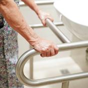 Old woman holding handrail next to bathroom sink