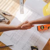 Contractor and client shaking hands above desk with paperwork on it