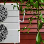 Electric heat pump against exterior wall of red residential home