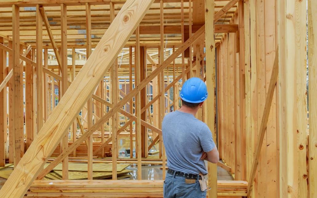 A home builder in a blue hard hat looks over work at a construction site