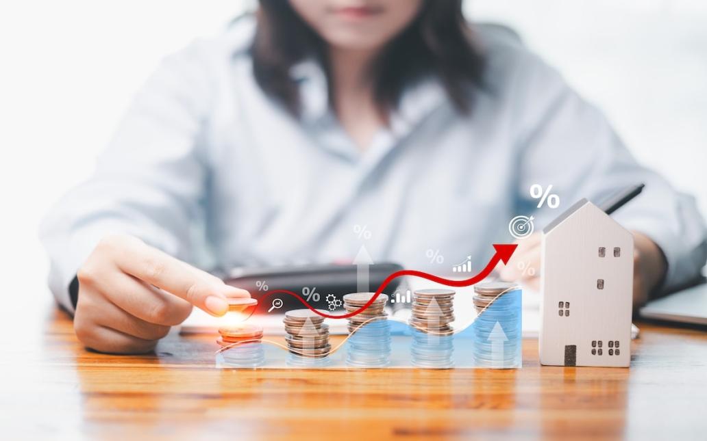 Coins are placed in ascending order from left to right. At the end of the row is a wooden model home, showing price changes in the housing market.