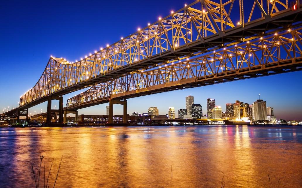 A bridge in New Orleans is illuminated at night with the city skyline behind it