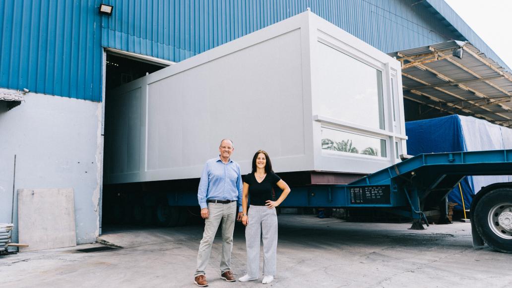 Man and woman by shipping truck with stackable modular apartment pod