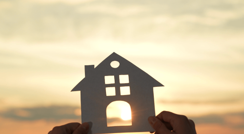 Hands holding up paper house cutout with sun shining through