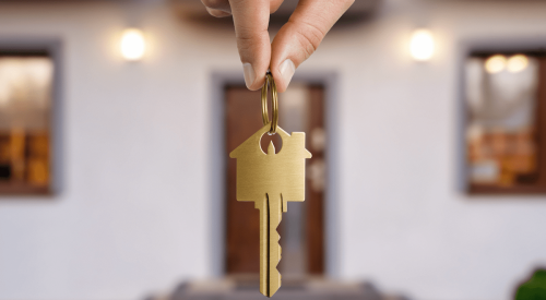  Hand holding house key in front of new home