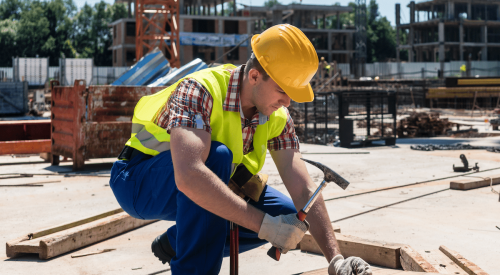 Construction worker on jobsite hammering nail into board