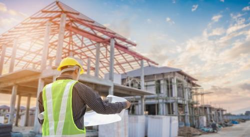 Construction worker looking over plans in front of row of under-construction homes