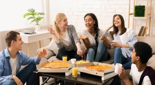 Members of Gen Z sit around coffee table laughing and sharing a meal 