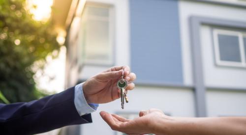 Individual takes the keys to a home that is in the background of image