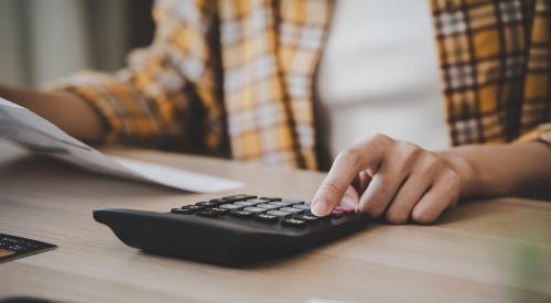 Renter sits at a table with calculator and papers, calculating monthly budget