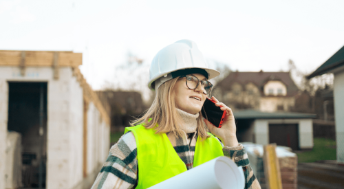 A woman construction worker holding a roll of house plans on a jobsite