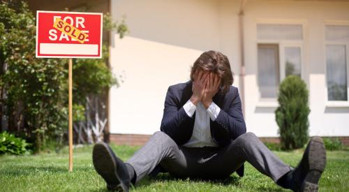 Young homebuyer sits on lawn head in hands 