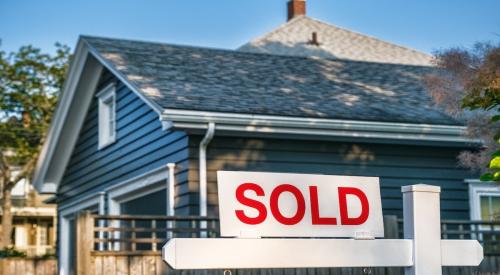 A blue starter home with a "sold" sign in the front yard