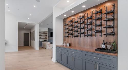 A display case of wine hangs over gray cabinetry in a modern home.