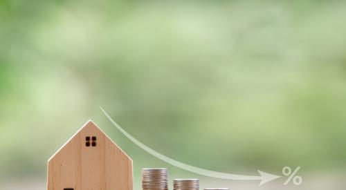 Wooden model house next to rows of coins in descending height order, showing a decrease in costs