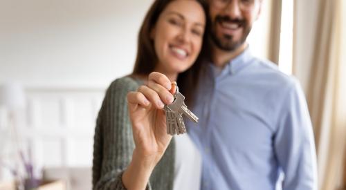 A young couple smiles and holds up a house key.