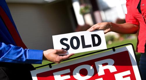 One person hands another person a sign reading "sold." A "For Sale" sign is in the background.