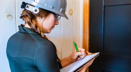 A woman in a gray hard hat takes notes at a jobsite