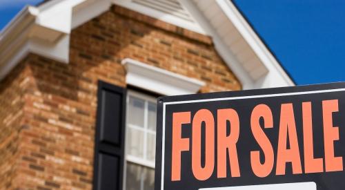 A "For Sale" sign sits in the front yard of a brick single-family home