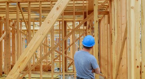 A home builder in a blue hard hat looks over work at a construction site