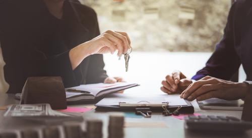 A selling agent hands over the keys to a buyer as they fill out paperwork