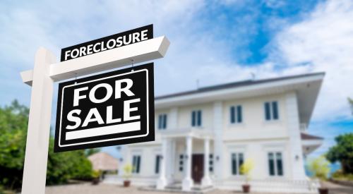 A black "Foreclosure" sign is posted in the front yard of a large white house