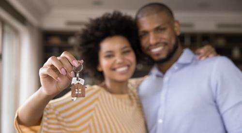 A Black couple smiles while holding up keys to their new home