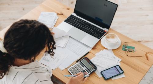 A renter looks over budget with laptop, bills, and calculator at a table