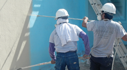 Two construction crew members painting a stucco wall on the jobsite