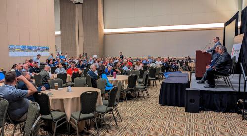 Professional builders in large room listening to speaker on stage