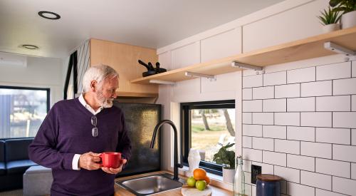 Senior drinking coffee in kitchen of Liv-Connected tiny home prototype