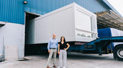 Man and woman by shipping truck with stackable modular apartment pod