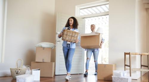 Two smiling Millennial friends moving into their home