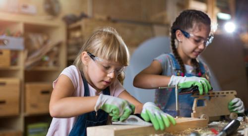 Two girls in a wood workshop planing and sanding their woodworking projects