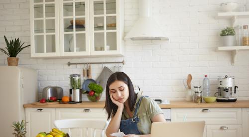 Young woman sitting in kitchen looking sadly at her budget