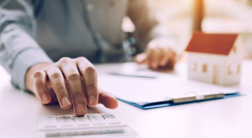 Person using calculator with home figurine in back