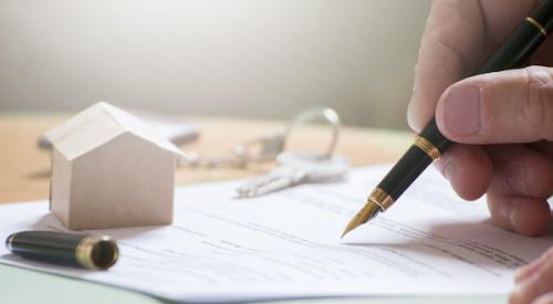 Person signing papers with house figurine in background