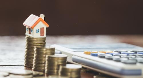 House figurine sitting on stacks of coins with nearby calculator