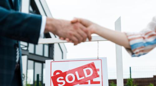 Broker and buyer shaking hands with a home sold sign behind them