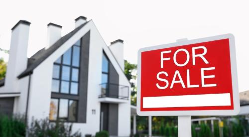 A house is in the background. In the foreground is a For Sale sign.