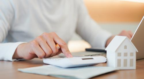 Person typing on calculator with home figurine